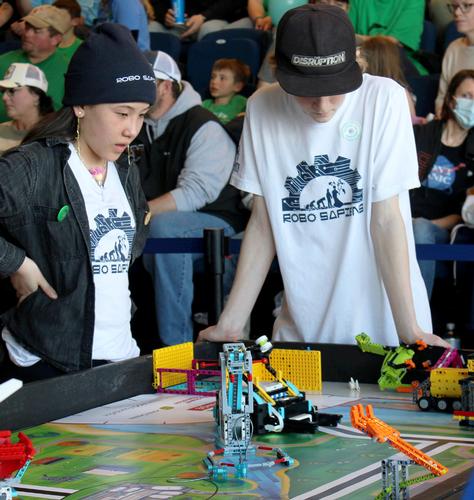 A photo by Charlie McLaughlin. Two youth look at a robot with questioning expressions.